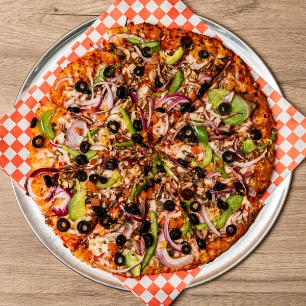 Curry On Pie's Indo-American pizza, topped with onions, peppers, olives, and mushrooms, on a metal tray.