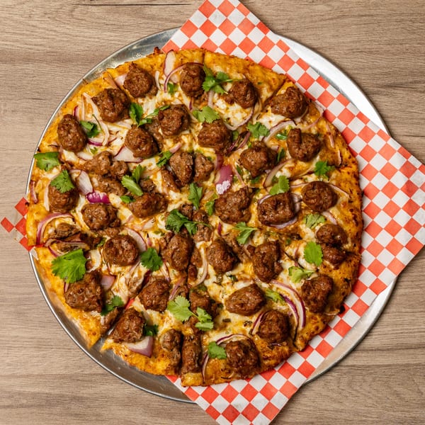 Curry On Pie's Indo-American pizza with meatballs, red onions, and cilantro on a checkered paper.